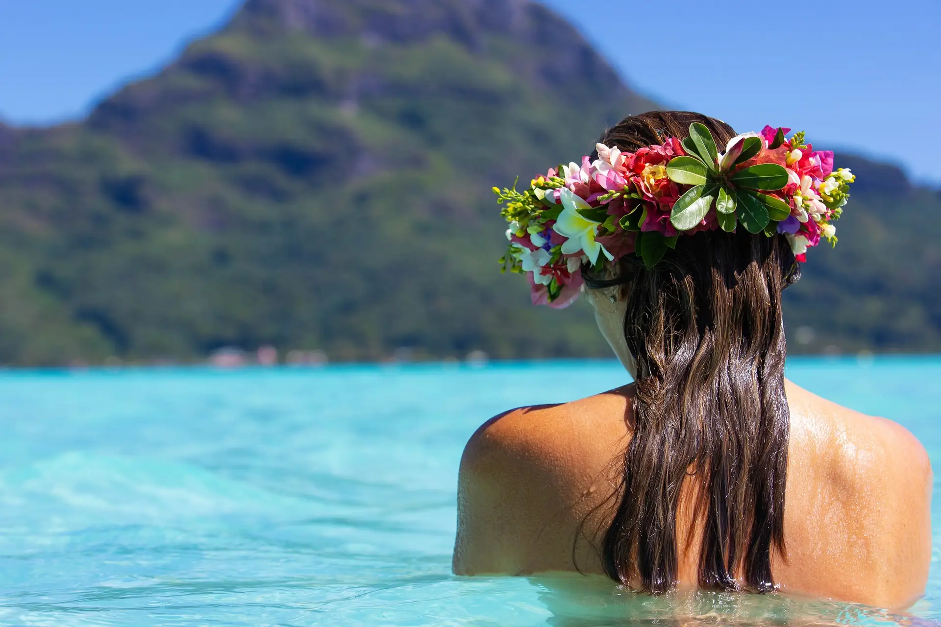Topless woman wearing colorful floral crown in turquoise ocean water on Bora Bora island